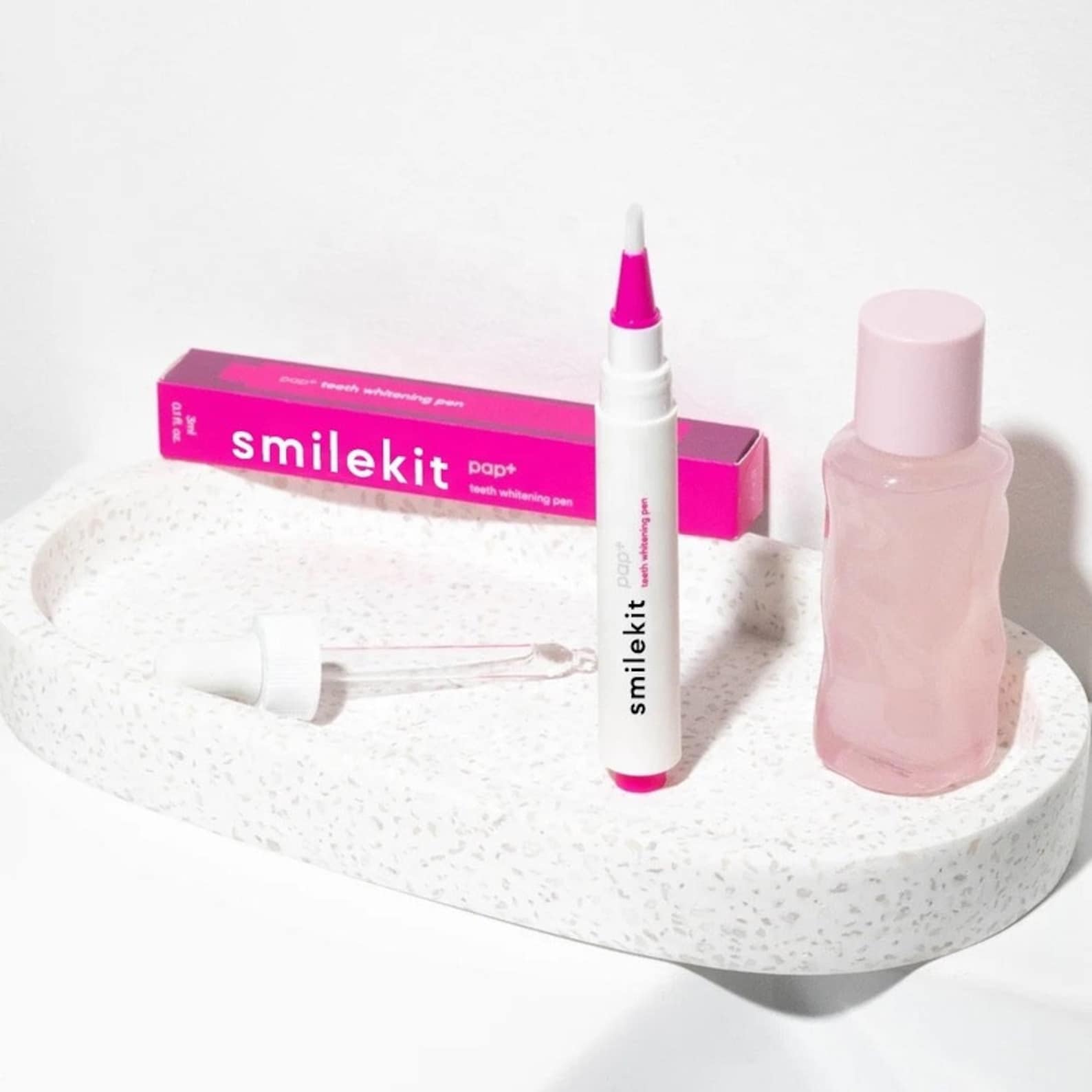 PAP+ Whitening Pen on a tray with a dropper bottle, featuring its compact, pink and white design.